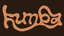 The word 'Kumba' meaning at home in Shona, written in a stylized, wavy orange-brown font against a solid dark brown background.
